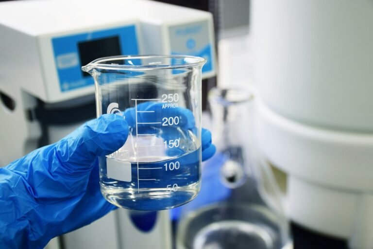 Mão com luva segurando béquer de laboratório de química